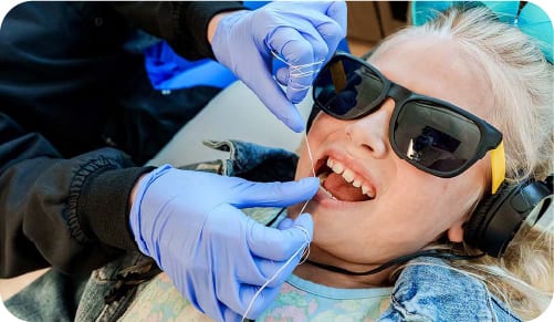 little girl getting her teeth flossed with glasses on