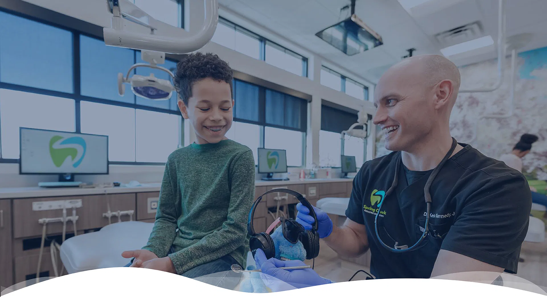 Dr. Kennedy with with a young boy patient at Spring Creek Pediatric Dentistry - offering headphones to wear during treatment for a more comfortable dental experience. 