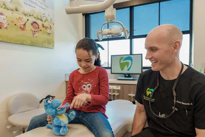 Young girl brushing teeth of stuffed animal with dentist